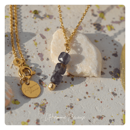 Détail du collier Vega en Iolite – perles facettées violet foncé, chaîne plaqué or et médaillon gravé L’Harmonie Précieuse sur fond minéral
