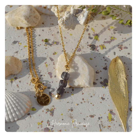 Collier Vega en Iolite – chaîne fine plaqué or et médaillon signature L’Harmonie Précieuse, posé sur fond minéral naturel